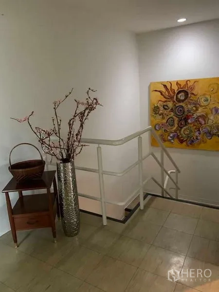 联排别墅 出租在Watthana, Bangkok - 楼梯平台，白色扶手、装饰画与高挑花瓶点缀。