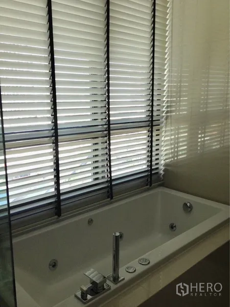 Condominium for rent in Khlong Toei, Bangkok - Windowed bathroom with a soaking bathtub and blinds for privacy.