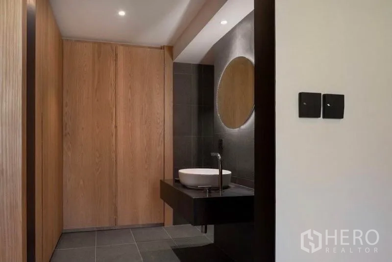 Condominium for rent in Phaya Thai, Bangkok - Modern bathroom with round mirror, vessel sink and wood-paneled storage.