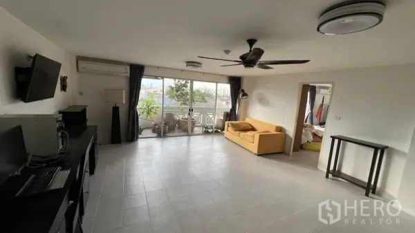 Condominium for sale in Wang Thonglang, Bangkok - Bright tiled living room with ceiling fan opening to a deep balcony with greenery in a Wang Thonglang condo.