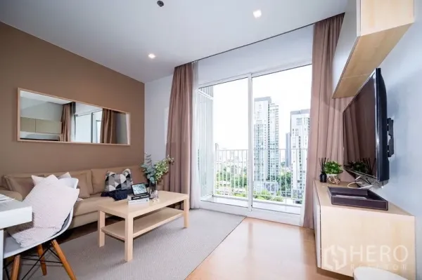 公寓 出租或出售在Watthana, Bangkok - 温馨客厅配沙发与镜面墙，推拉门连接阳台，远眺高楼天际线
