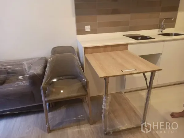Condominium for sale in Din Daeng, Bangkok - Foldable wooden dining table beside the kitchenette with wrapped chairs and sofa.