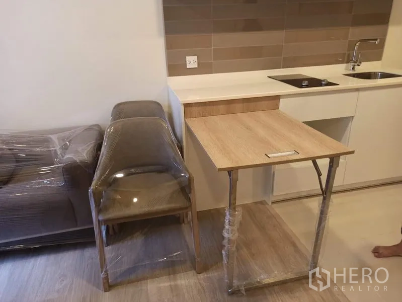 Condominium for sale in Din Daeng, Bangkok - Foldable wooden dining table beside the kitchenette with wrapped chairs and sofa.