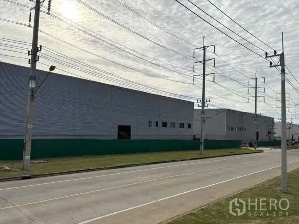 Factory for rent in Rayong - Long metal factory facade along a wide road with power lines in Pluak Daeng, Rayong.