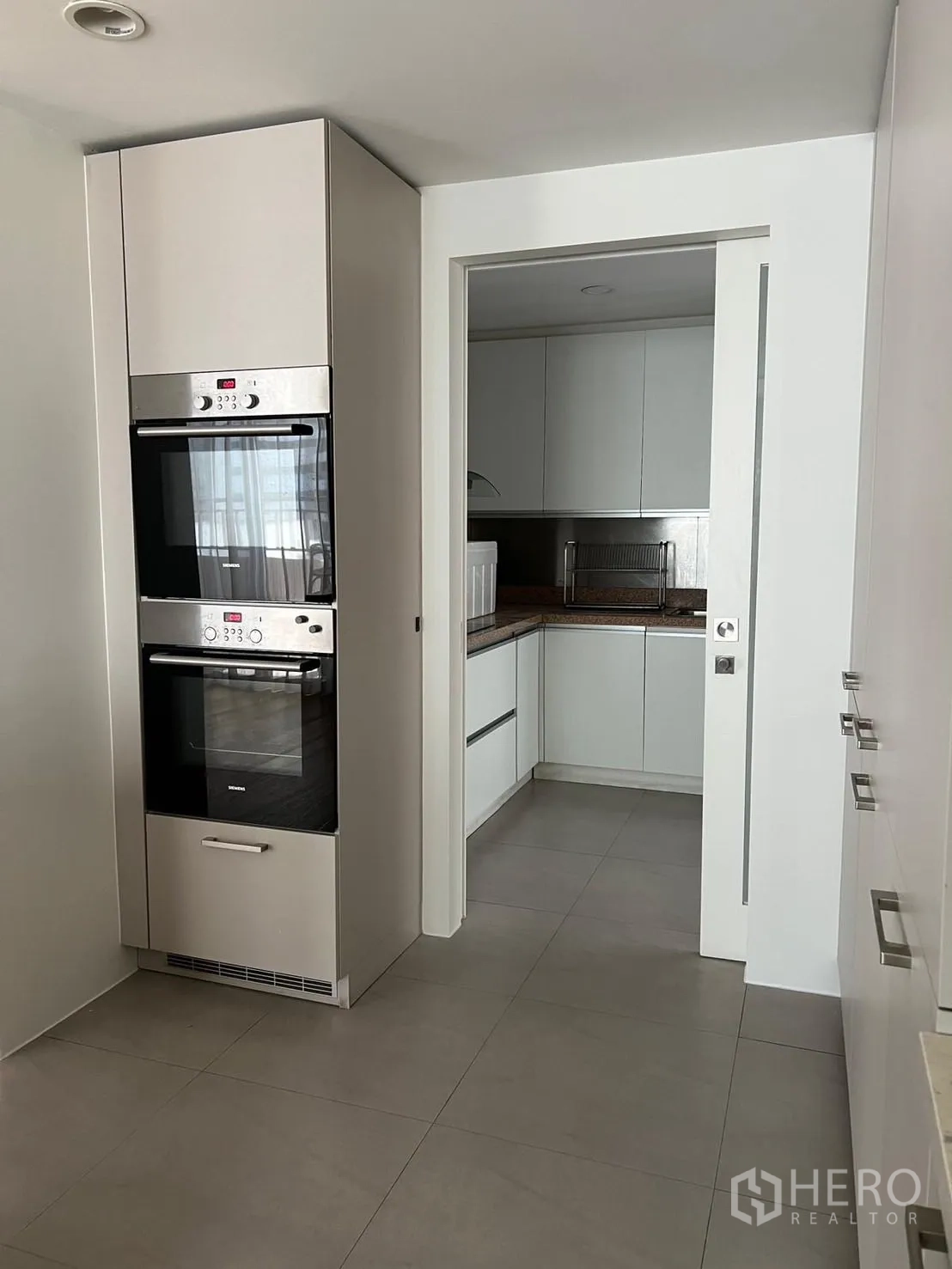 Condominium for rent or sale in Sathon, Bangkok - Modern kitchen with built-in double ovens and sliding door to a prep area.