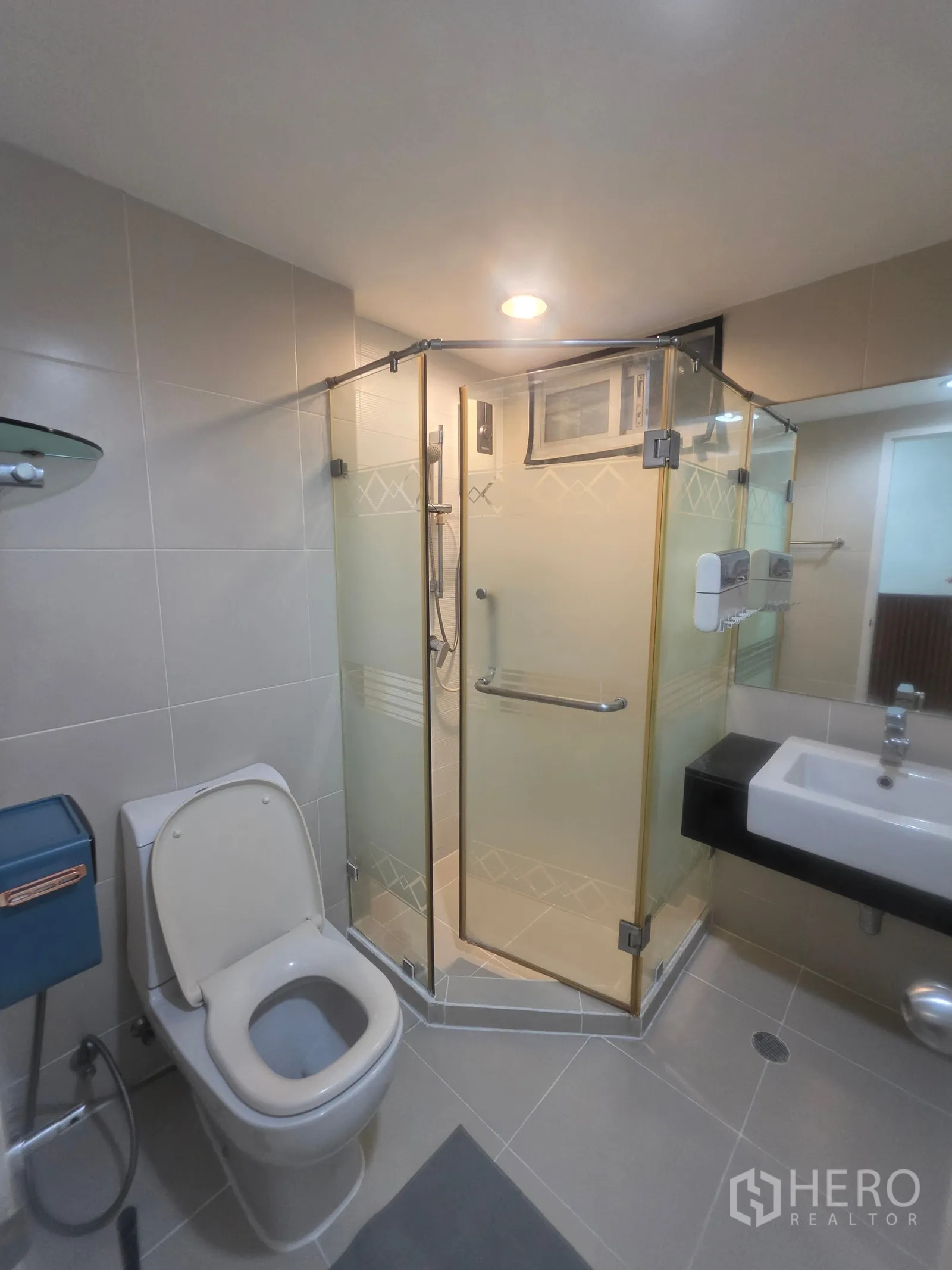 Condominium for rent in Huai Khwang, Bangkok - Bright bathroom with glass-enclosed corner shower, toilet, and wall sink.