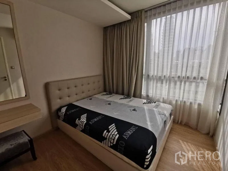Condominium for rent or sale in Watthana, Bangkok - Corner bedroom with floor-to-ceiling windows and city skyline view through sheer curtains.
