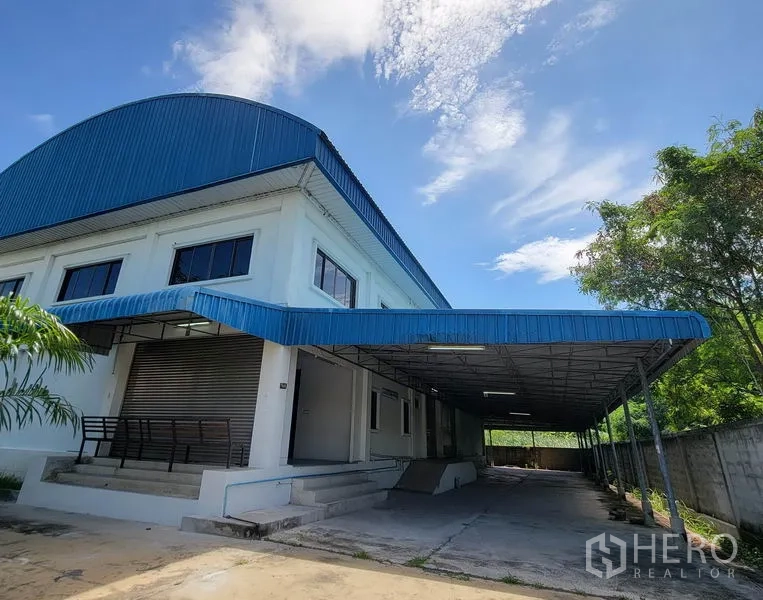 Warehouse for rent in Sam Phran, Nakhon Pathom - White warehouse with blue metal roof, covered loading dock and ramp under a clear sky in Sam Phran.