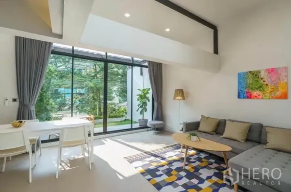 联排别墅 出租在Khlong Toei, Bangkok - 客厅挑高空间，落地玻璃墙与灰色转角沙发