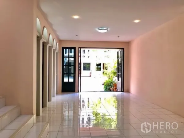 Townhouse for rent in Watthana, Bangkok - Ground floor hall with glossy white tiles, arched doorways and double glass doors to a courtyard.
