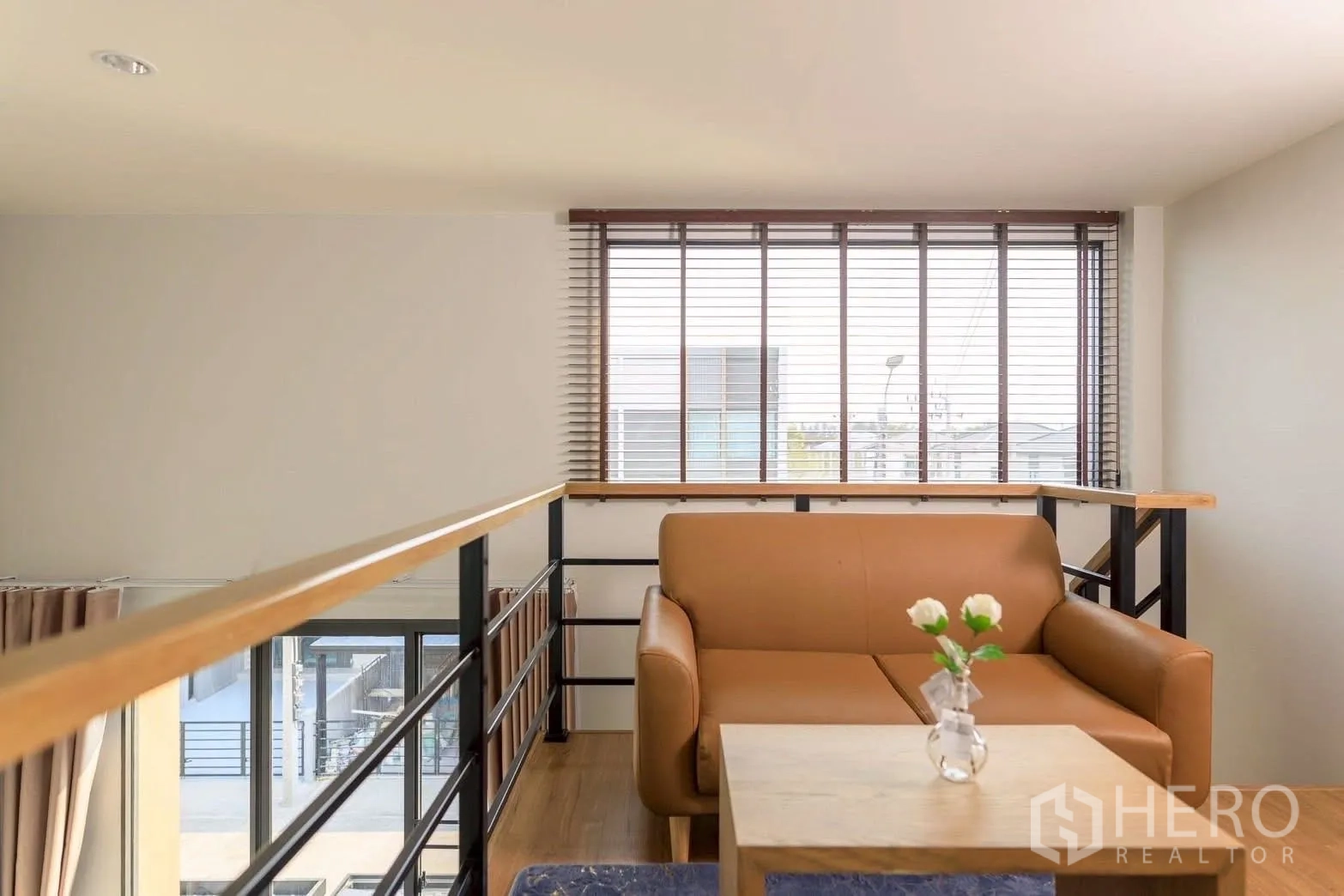 Townhouse for rent or sale in Bang Phli, Samut Prakan - Cozy mezzanine lounge with leather sofa, wood railing and large window blinds in a modern townhouse.
