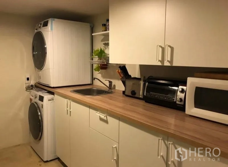 Townhouse for rent in Khlong Toei, Bangkok - Utility pantry with stacked washer and dryer, sink, microwave and storage cabinets.