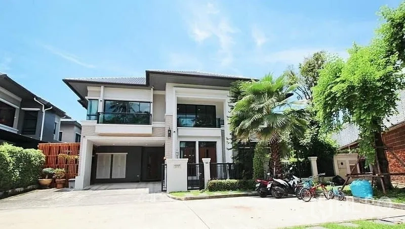 Detached House for rent in Bang Khae, Bangkok - Modern two-storey detached house with balcony, driveway and tropical trees in Bang Khae under a blue sky.