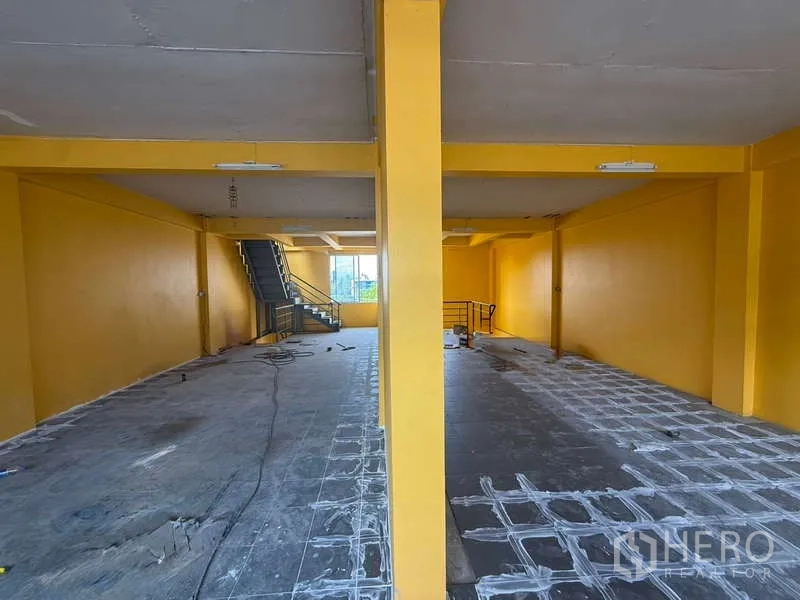 Home Office for rent in Khlong Toei, Bangkok - Expansive open floor with yellow columns, staircase and partial tiling suitable for workstations.
