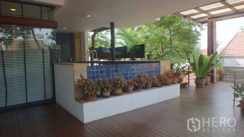 Detached House for rent in Watthana, Bangkok - Covered terrace with wooden decking, planter boxes, and a bar counter amid greenery.