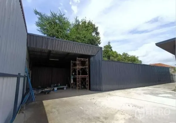 Warehouse for rent in Prawet, Bangkok - Metal-clad warehouse exterior with covered loading bay, scaffolding, and wide concrete forecourt.