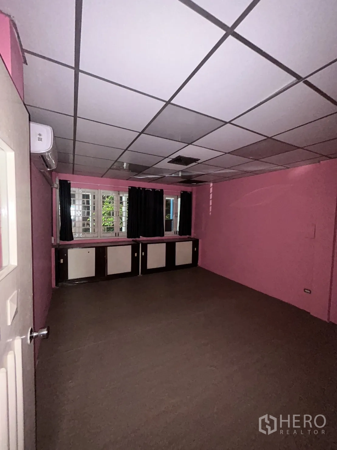 Shophouse for rent in Khlong Toei, Bangkok - Pink room with window cabinets, air conditioner, and grid ceiling panels.