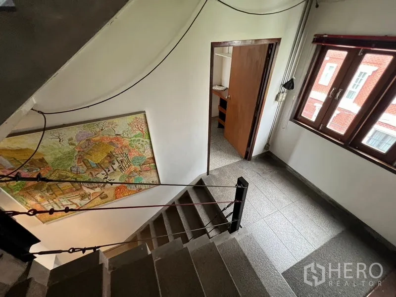 办公空间 出租在Watthana, Bangkok - 楼梯平台带窗与墙面装饰画，磨石地面通往办公室楼层。