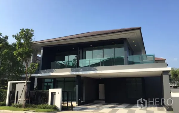 Detached House for sale in Bang Kapi, Bangkok - Modern two-storey detached house in Hua Mak, Bang Kapi with glass balcony, floor-to-ceiling windows, gated entrance and a covered carport on a sunny day.