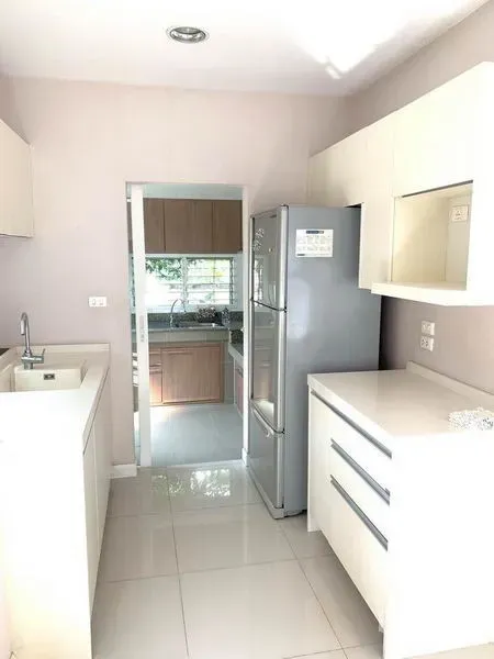 Detached House for rent in Bang Kapi, Bangkok - Clean white kitchen with built-in cabinets and stainless refrigerator leading to a second Thai kitchen.