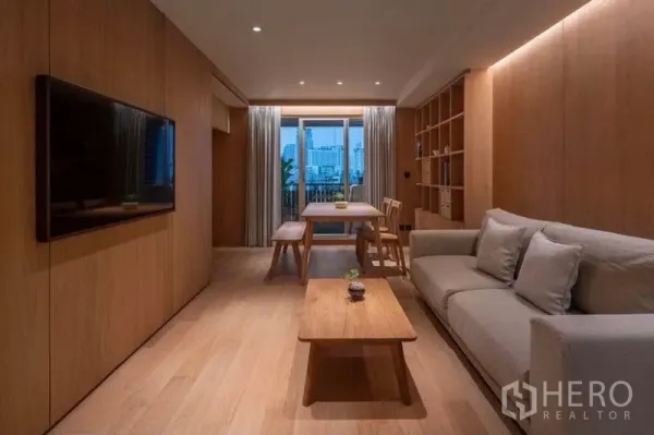 Condominium for rent in Phaya Thai, Bangkok - Warm wood-toned living room with sofa, TV wall, dining table and balcony city view at dusk.