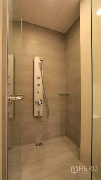 Condominium for rent - Glass shower enclosure with multi‑jet panel and light stone tiles.