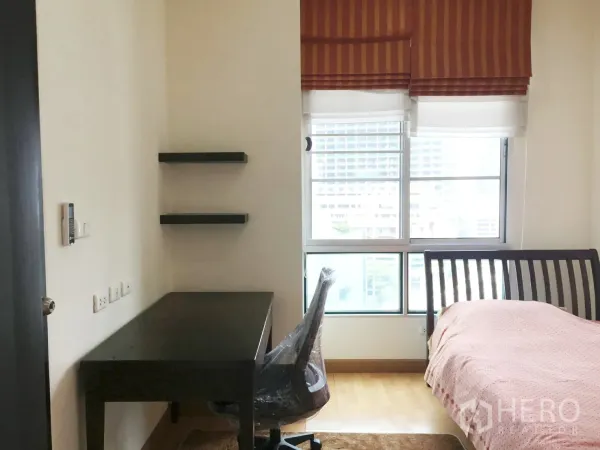 Condominium for rent in Khlong Toei, Bangkok - Second bedroom with work desk, wall shelves and natural light from the window.