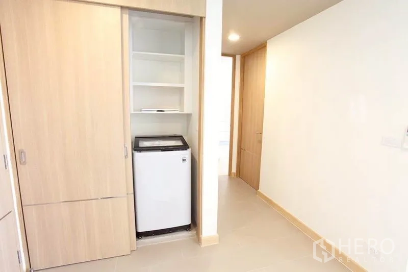 Condominium for rent in Watthana, Bangkok - Built-in light-wood closet with shelving and a top-load washing machine in the hallway.