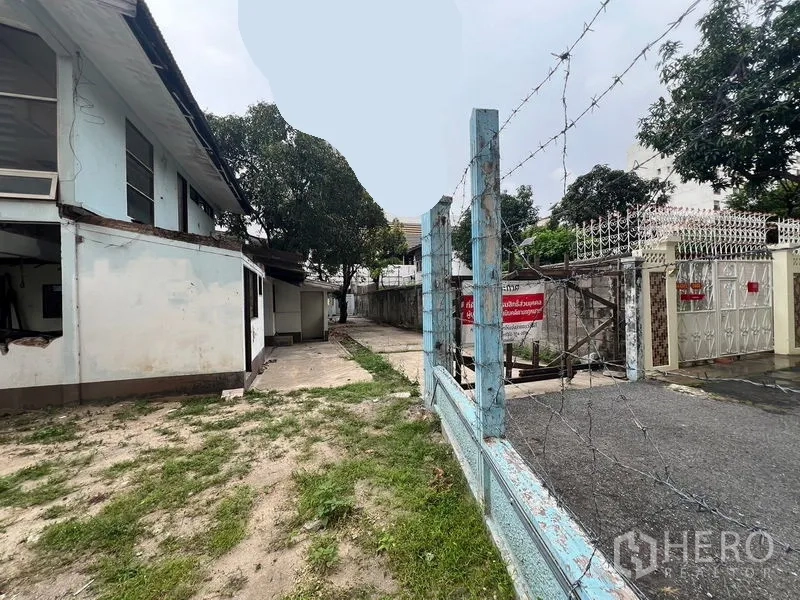 Land for rent in Watthana, Bangkok - Entrance area with barbed-wire fence and driveway into the property.