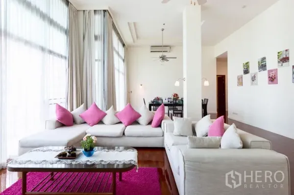 Condominium for rent in Bang Rak, Bangkok - Light-filled lounge with oversized sofas, pink cushions and full-height curtains.