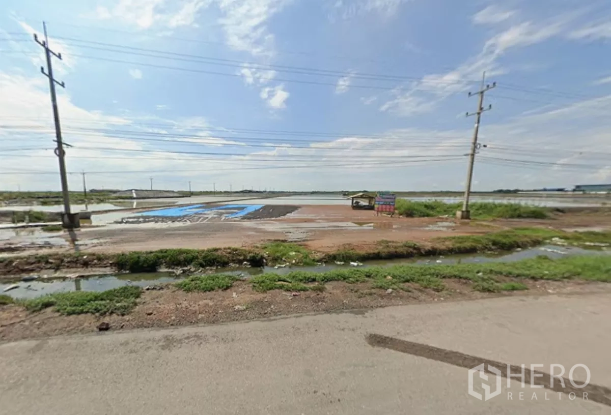 Land for sale in Mueang Samut Sakhon, Samut Sakhon - Roadside view of expansive salt-field land with utility poles, drainage ditch and wide sky along Rama 2 corridor.