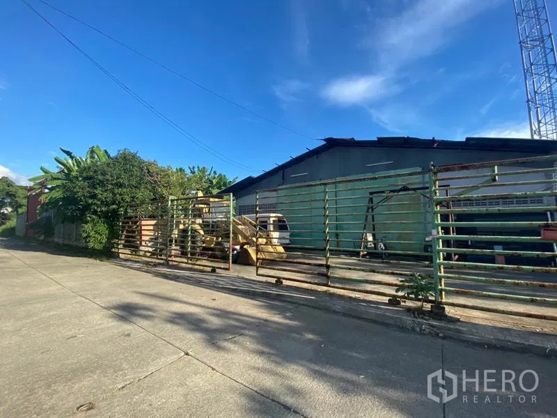 Warehouse for rent in Suan Luang, Bangkok - Main façade behind extended metal gates, revealing loading yard and equipment areas.