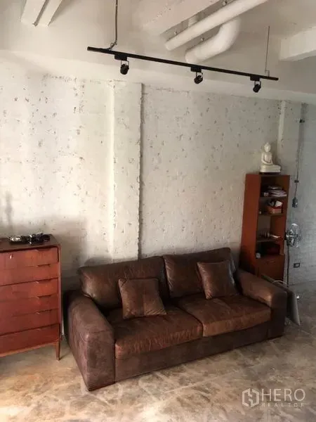 联排别墅 出售在Wang Thonglang, Bangkok - 舒适休闲角，棕色皮沙发、白色质感砖墙与轨道灯。