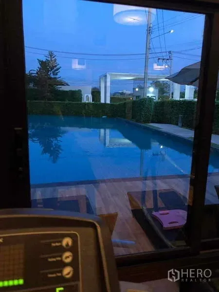Detached House for rent or sale in Prawet, Bangkok - Community swimming pool and fitness view at dusk seen through a glass window.