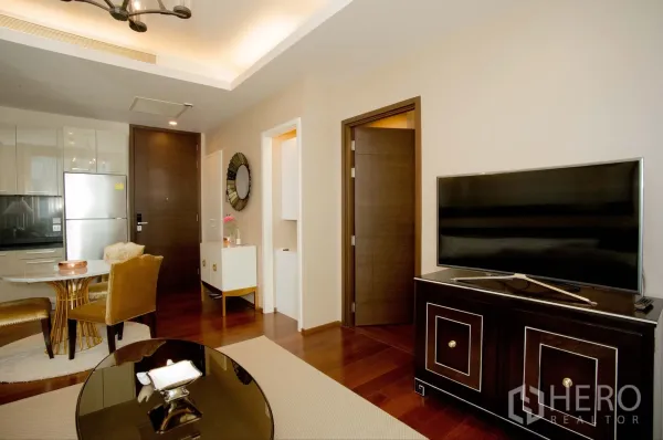 Condominium for rent in Watthana, Bangkok - Entry and living area view with TV console, wooden floors, and a dining table beside the compact kitchen.