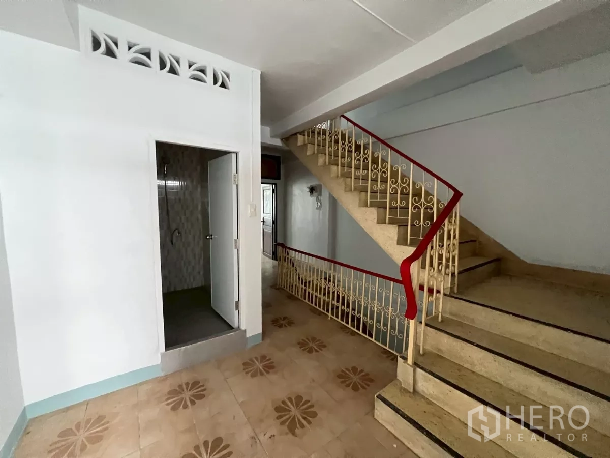 Shophouse for rent in Khlong Toei, Bangkok - Stair landing with red handrail and decorative metal balustrade beside bathroom entrance.