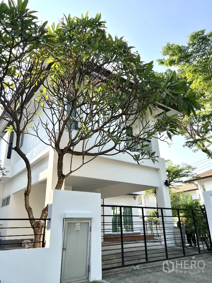 独立式住宅 出租或出售在Saphan Sung, Bangkok - 房屋前角度，可见有顶车棚、黑色大门与鸡蛋花树。