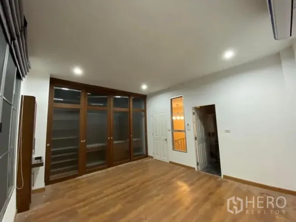 Townhouse for rent in Lat Phrao, Bangkok - Upper bedroom with wood flooring, built-in glass-front wardrobes and recessed lights.