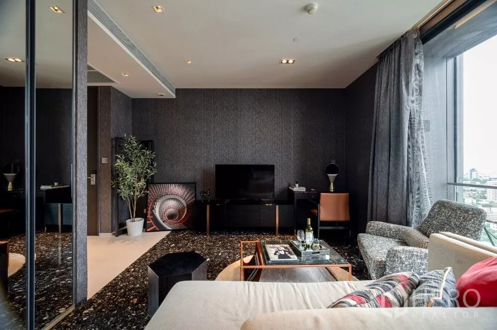 Condominium for rent or sale in Khlong Toei, Bangkok - Living room with TV console, armchairs and large windows framing skyline views.