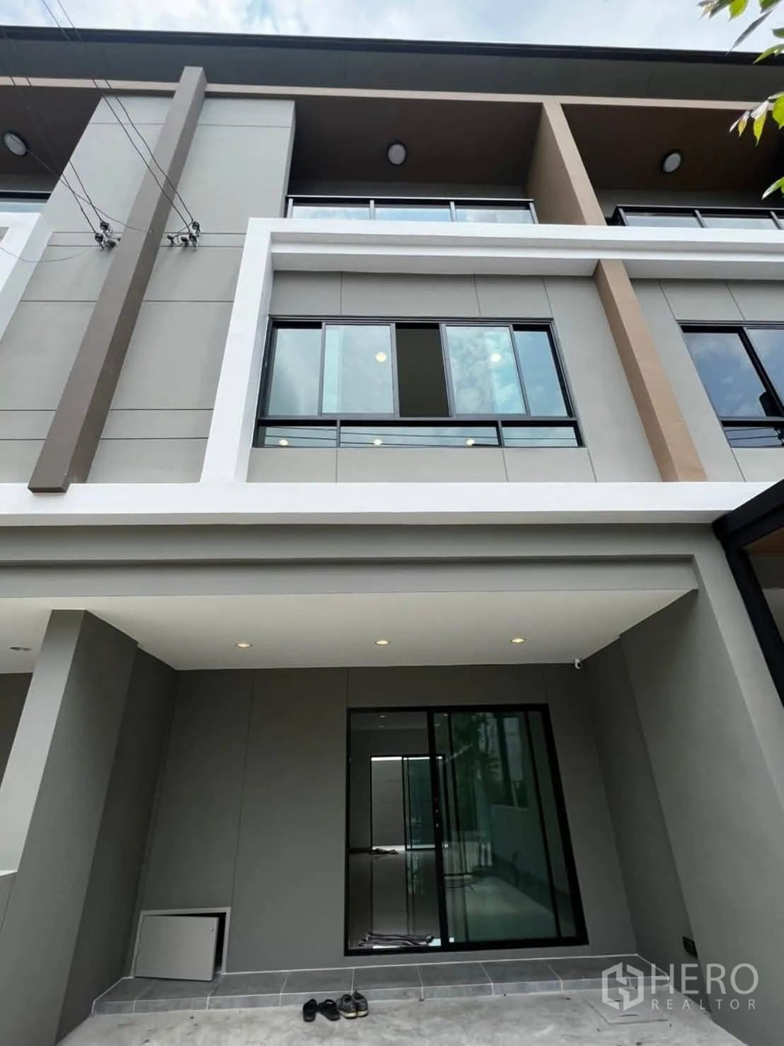 ทาวน์เฮาส์ ให้เช่าในBang Khen, Bangkok - ด้านหน้าทาวน์เฮ้าส์สมัยใหม่หลายชั้น หน้าต่างบานใหญ่และระเบียงเหนือที่จอดรถ