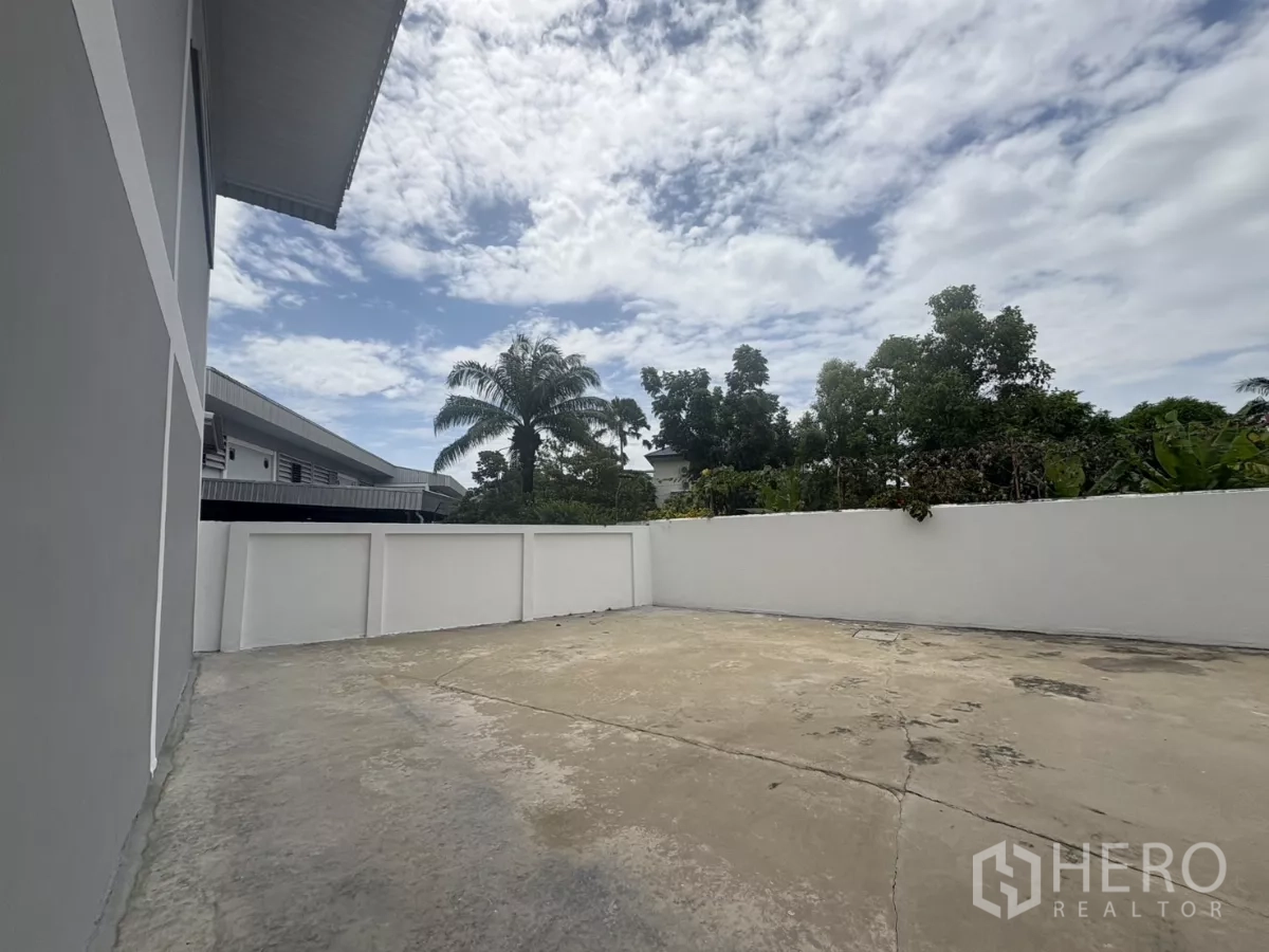 Factory for rent in Phra Samut Chedi, Samut Prakan - Side yard showing wide concrete apron and greenery behind the wall.