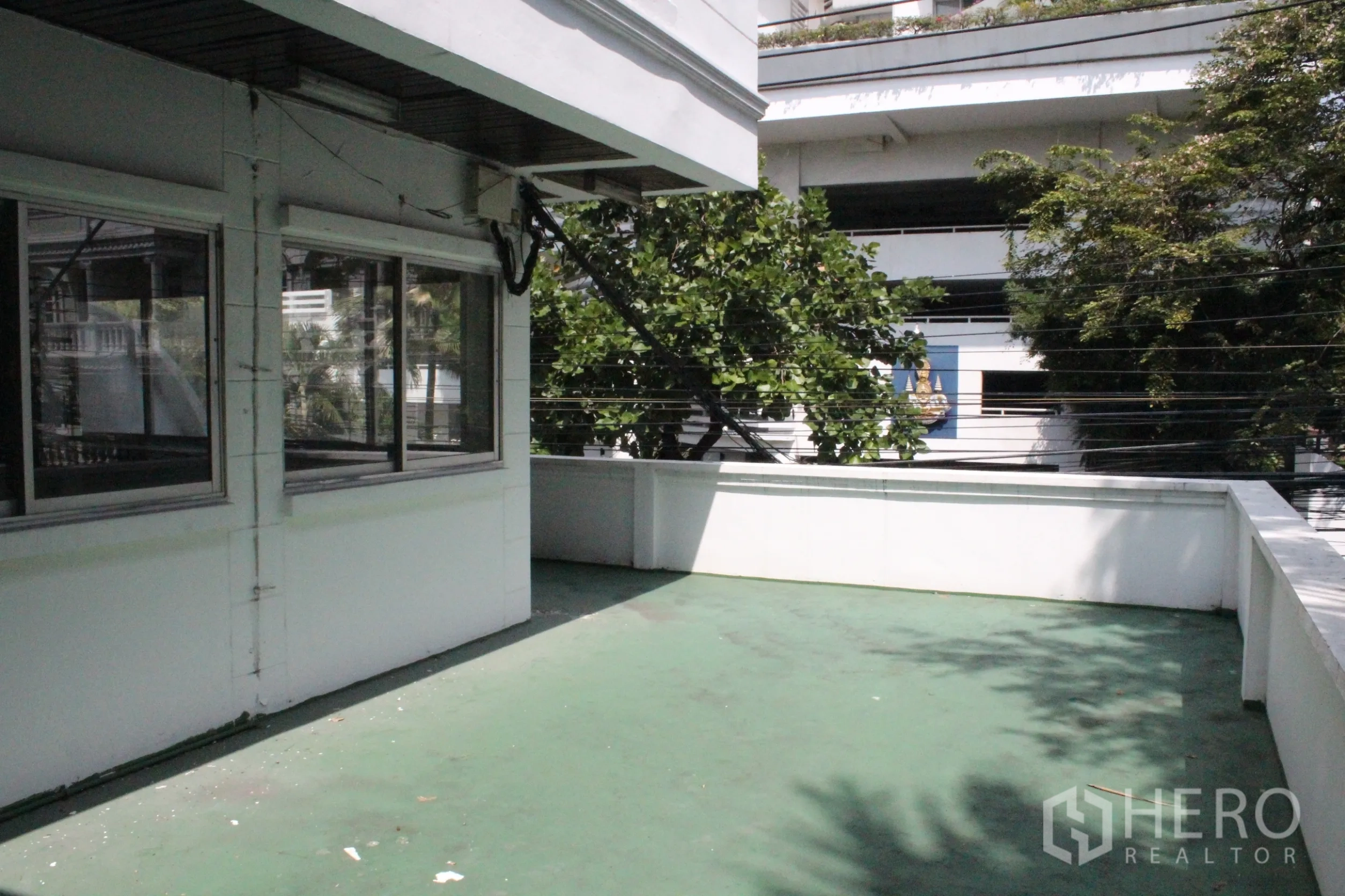 Home Office for rent in Khlong Toei, Bangkok - Large rooftop terrace with green flooring beside a white facade and urban views.