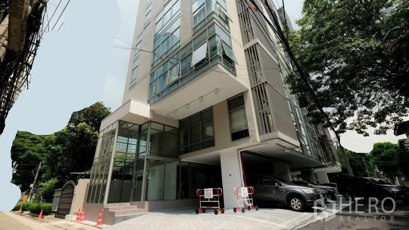办公空间 出租在Bang Rak, Bangkok - 是隆区现代低层办公楼外观，玻璃立面、车道与树荫停车位。