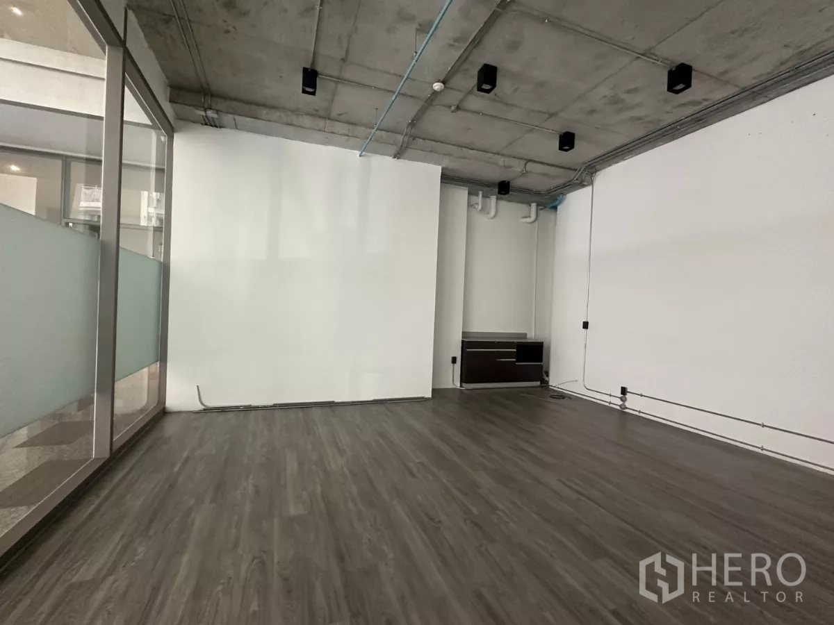 Retail Space for rent - Wide interior shot with track lighting, glass wall, wood-look vinyl flooring and visible utility conduits.