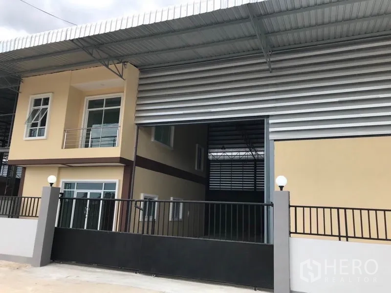 Warehouse for rent in Samut Sakhon - Warehouse exterior with wide roller shutter, two-storey office wing and gated entrance under a large roof canopy.
