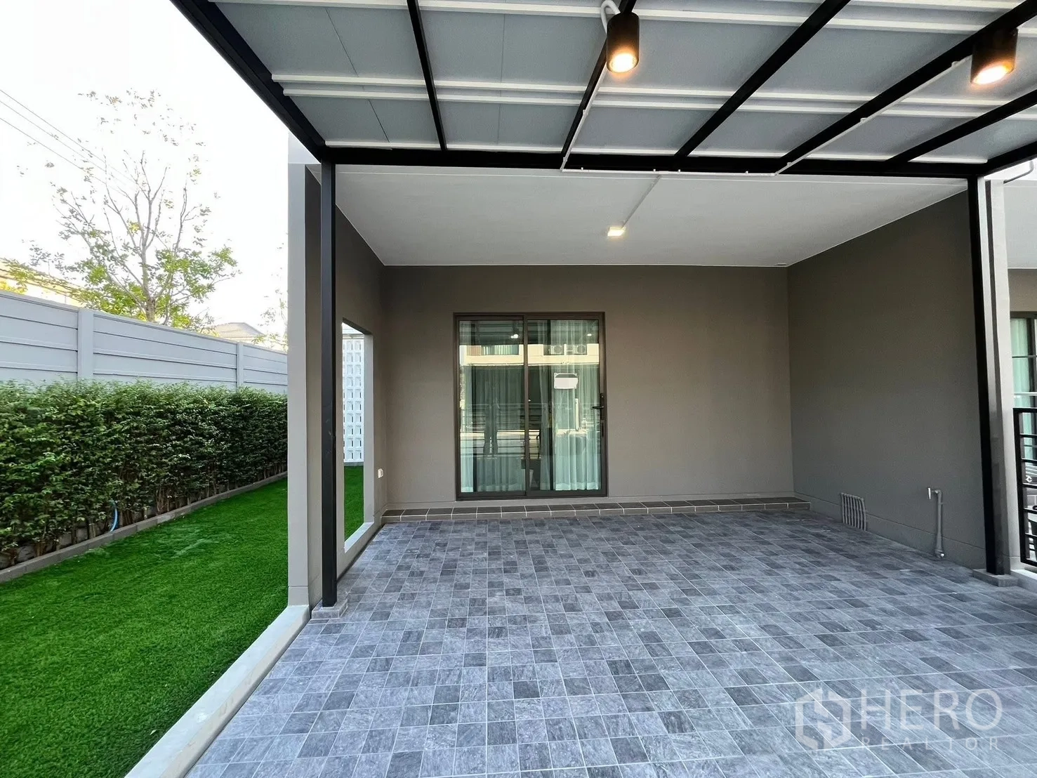 Townhouse for rent in Bang Phli, Samut Prakan - Covered carport with gray tiled floor and ceiling lights adjoining the lawn and sliding glass door.