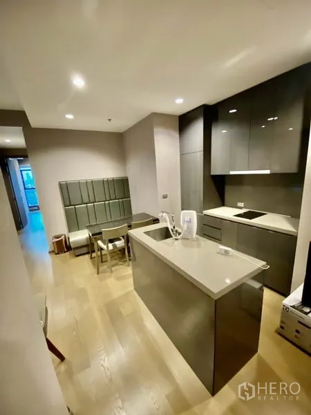 Condominium for rent or sale in Bang Rak, Bangkok - Contemporary kitchen with island counter, glossy cabinets, induction cooktop and a compact dining nook in a Bang Rak condo.