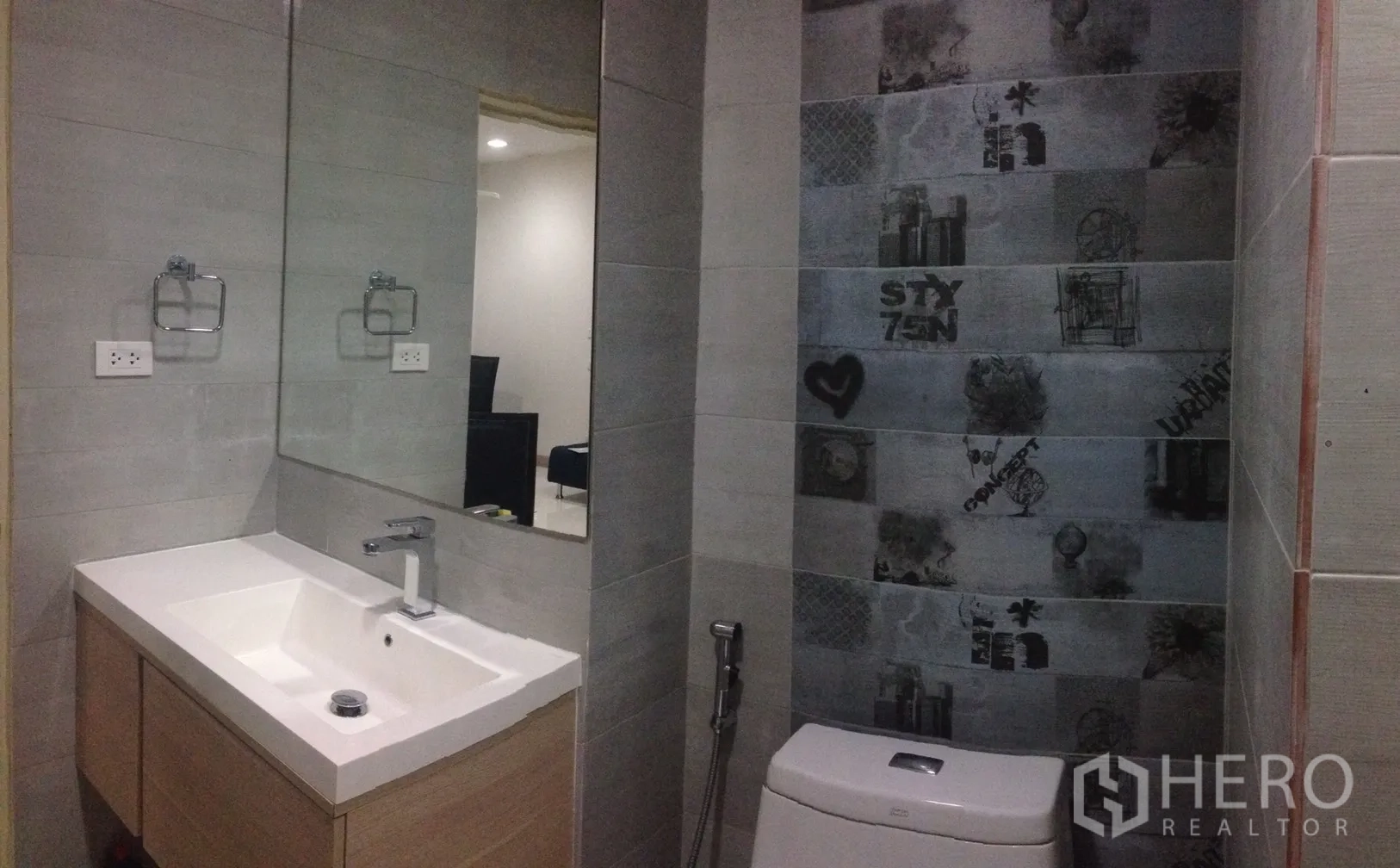 Condominium for rent in Phaya Thai, Bangkok - Modern bathroom featuring a large mirror, vanity sink, toilet and patterned tile accent wall.