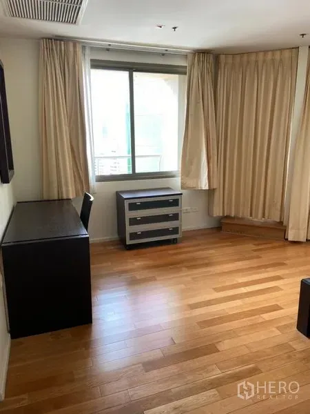 Condominium for rent in Khlong Toei, Bangkok - Bright room with a window, desk, drawers, and light curtains over wooden flooring.