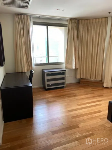 Condominium for rent in Khlong Toei, Bangkok - Bright room with a window, desk, drawers, and light curtains over wooden flooring.